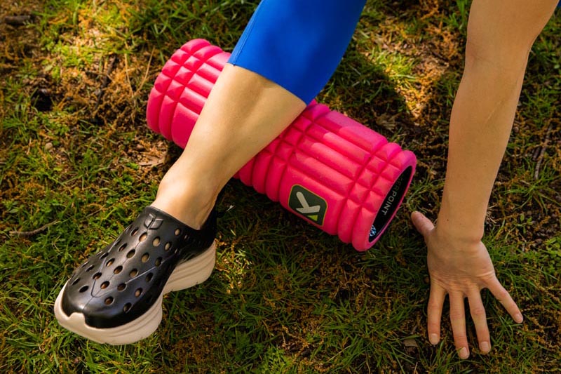 Person rolling their calf with a pink foam roller outdoors on grass
