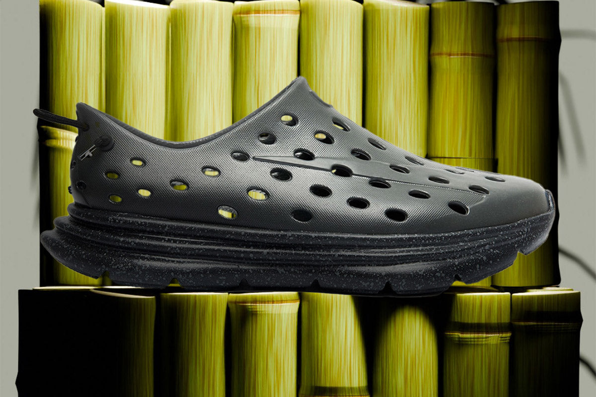 Side view of a charcoal-black perforated running shoe against green bamboo stalks