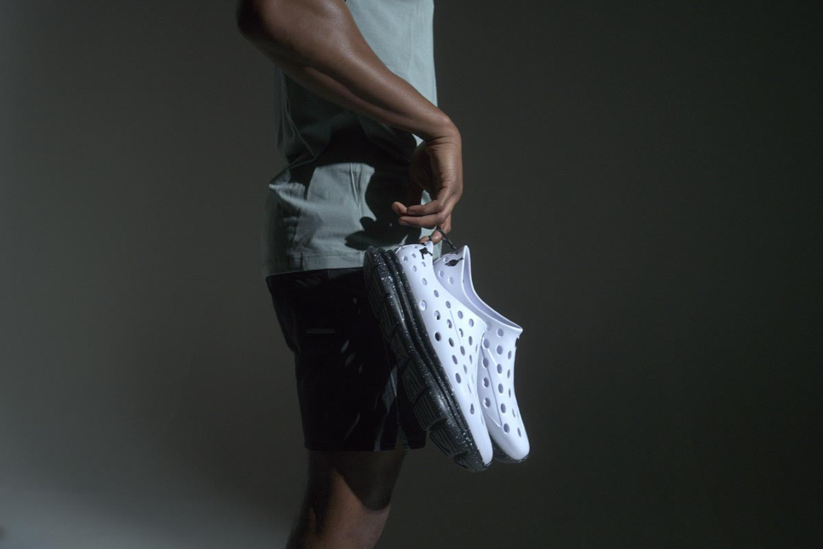 Person carrying white perforated athletic shoes against a dark background
