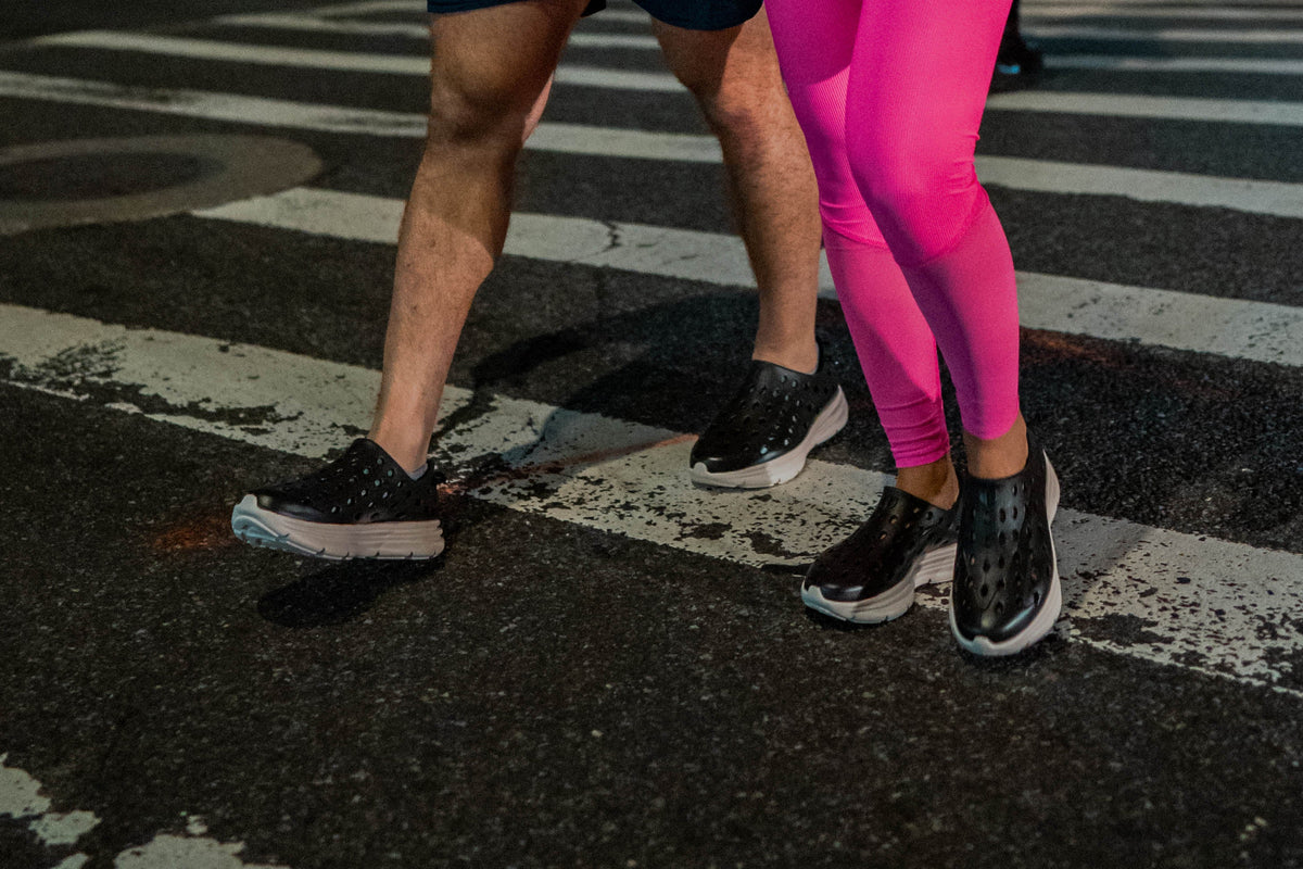 Two people walking across a painted street crossing in black athletic shoes