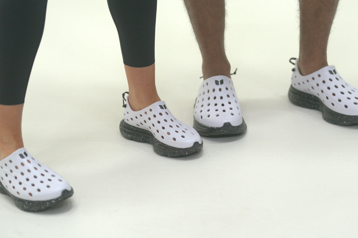 Front view of white perforated slip-on shoes showcasing black soles with a white background