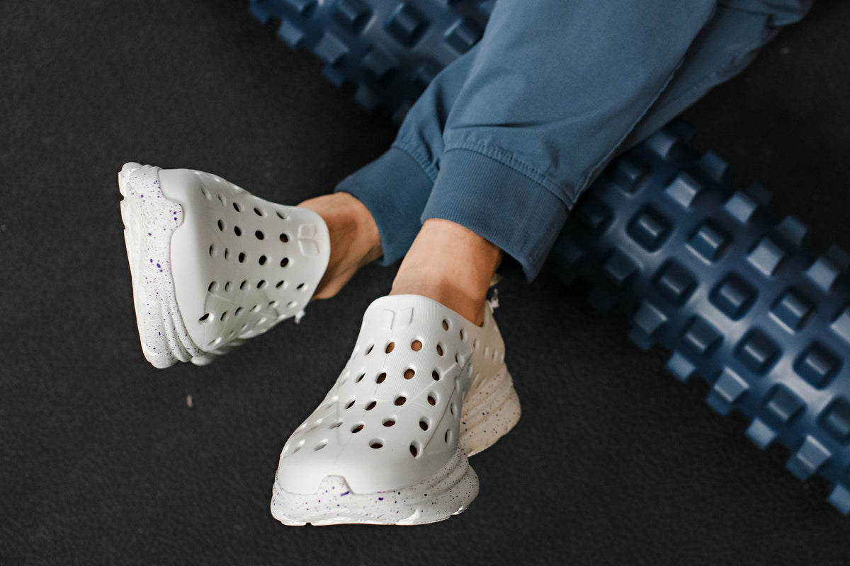 Close view of white recovery shoes showcasing perforated uppers with a black floor and blue textured mats