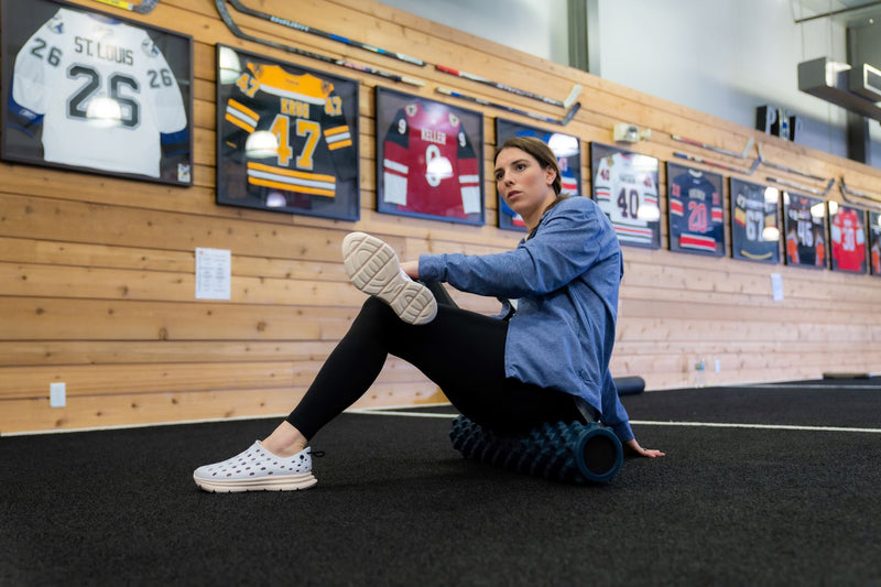 Woman using a textured foam roller for muscle relief in a gym with framed sports jerseys