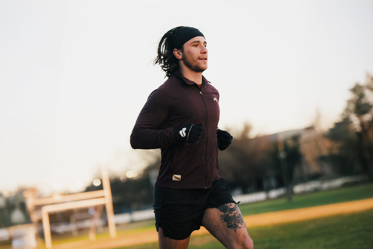 Runner jogging outdoors on a grassy field in a dark athletic outfit