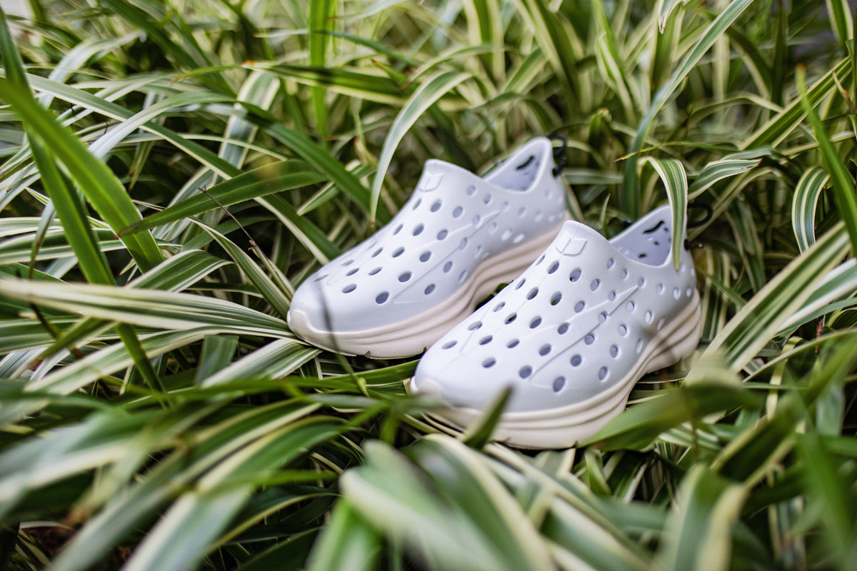Close-up of white recovery shoes showcasing perforated uppers with ornamental grass background