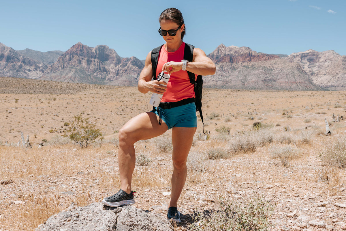 Woman hiking through a desert landscape while checking her watch