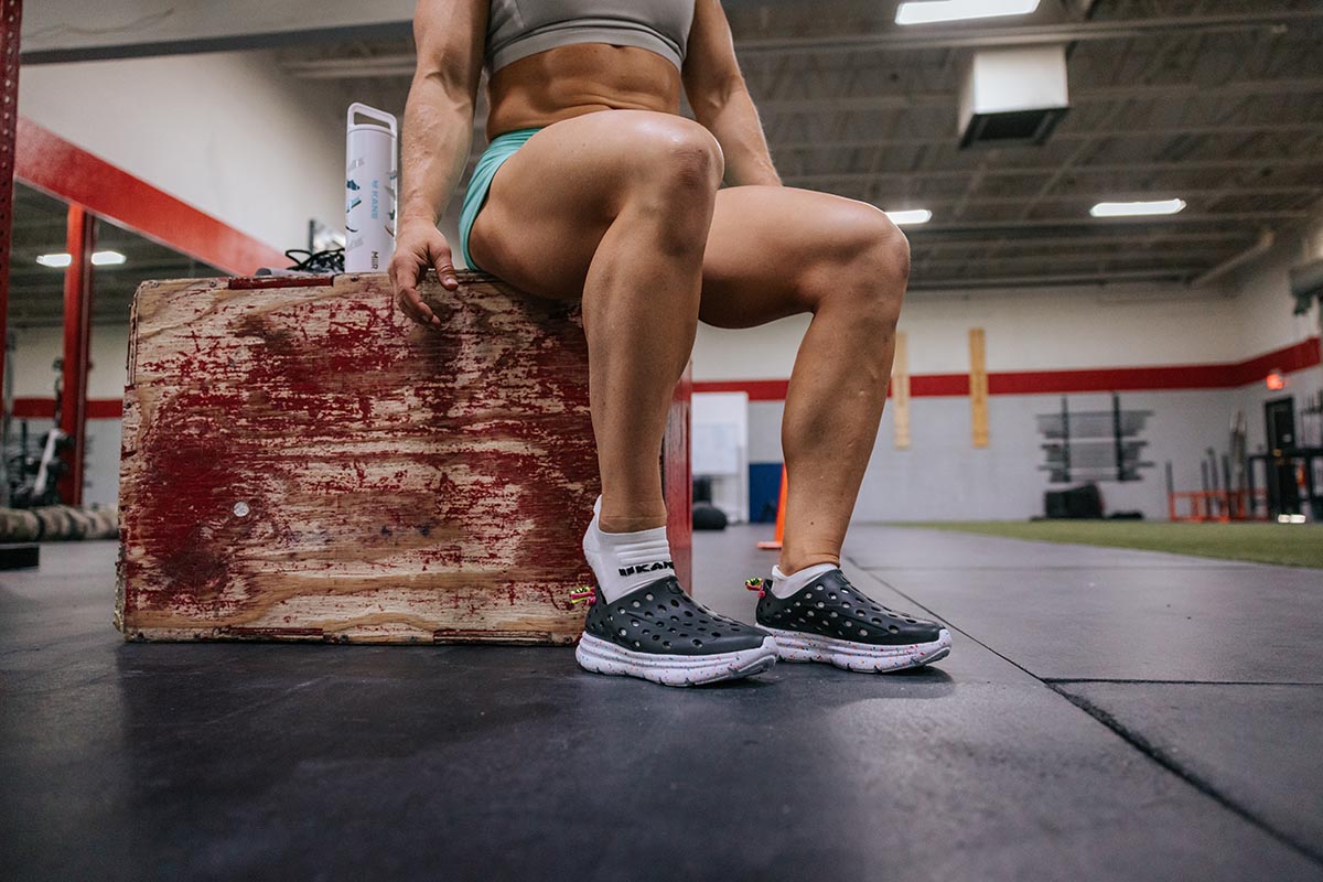 Person seated on a wooden box in a gym wearing black perforated clogs