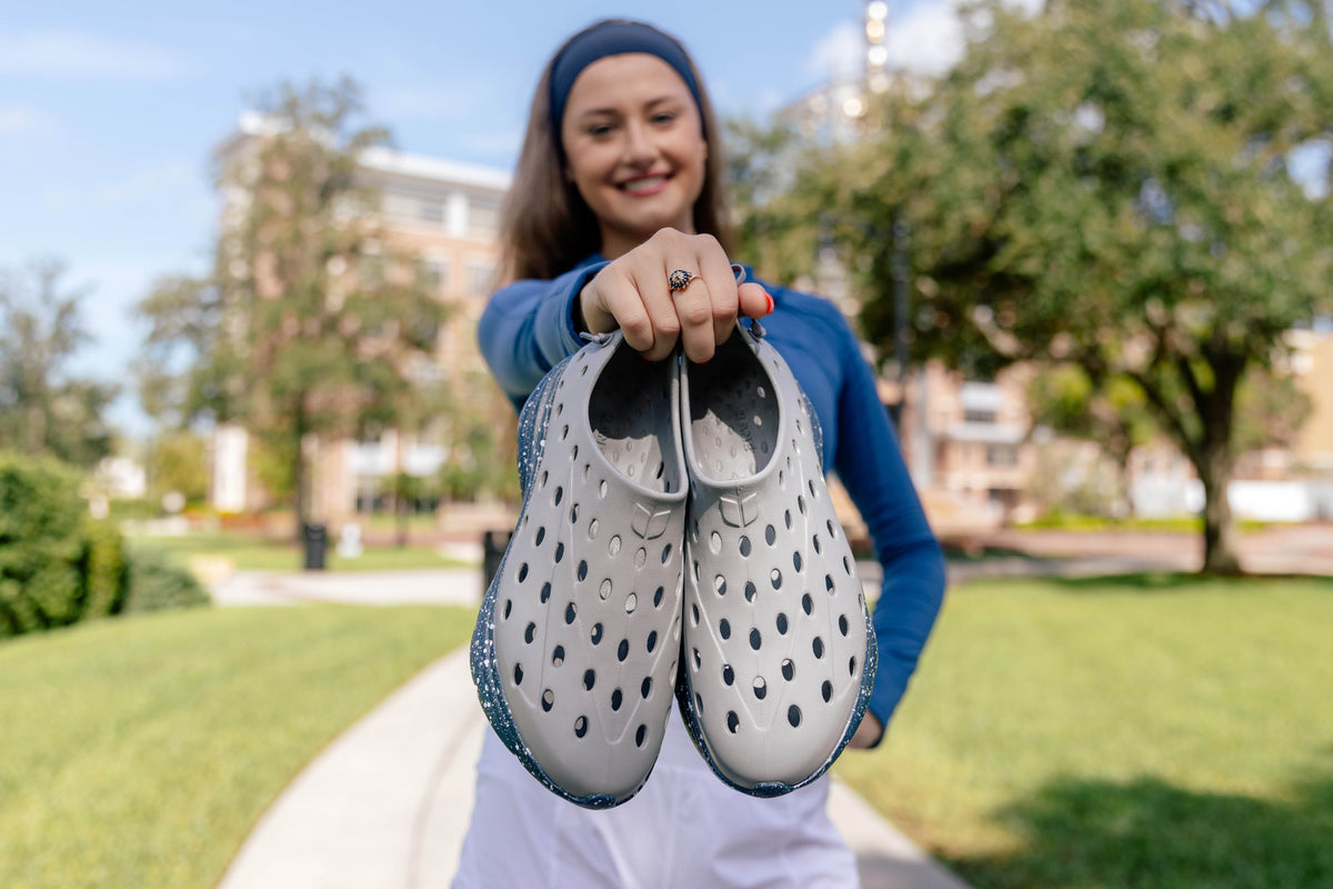 Woman holding gray recovery shoes on a sunny outdoor walkway