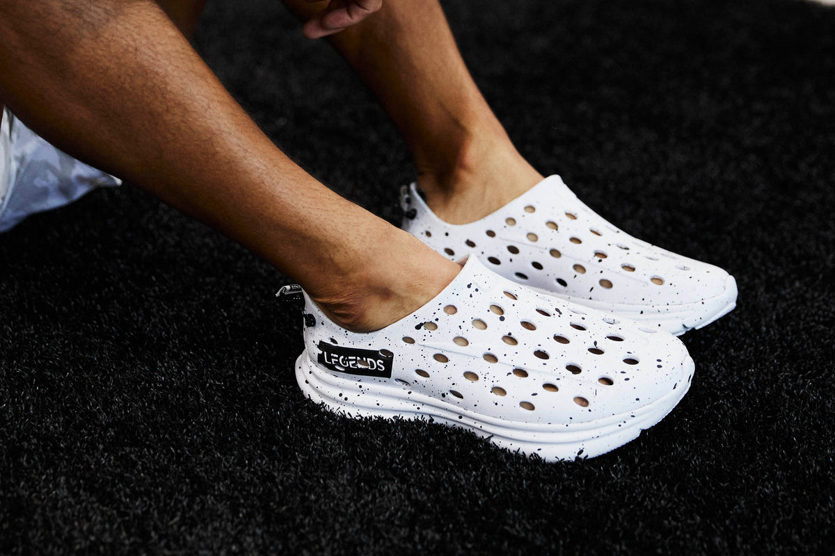 Side view of white perforated clogs showcasing ventilated uppers on feet against a black textured background