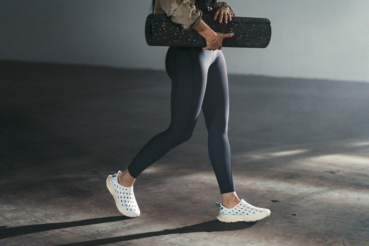 Person walking while carrying a rolled black exercise mat in a studio