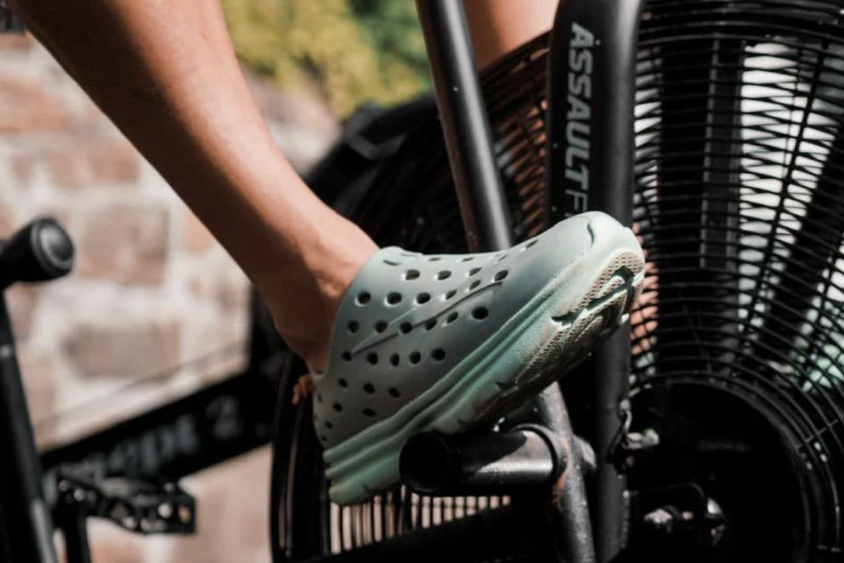 Person pedals an air bike wearing a gray-green perforated athletic shoe