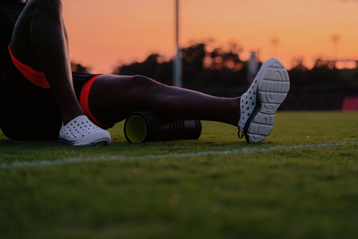 Athlete using a foam roller on a leg outdoors at sunset