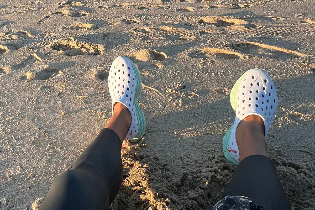Person wearing perforated water shoes while sitting on a sandy beach