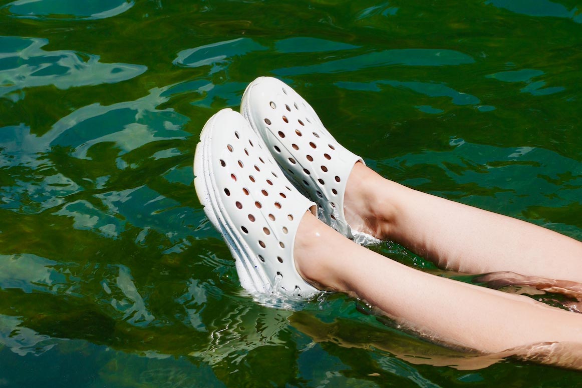 Person wearing white perforated clogs with feet submerged in rippling water
