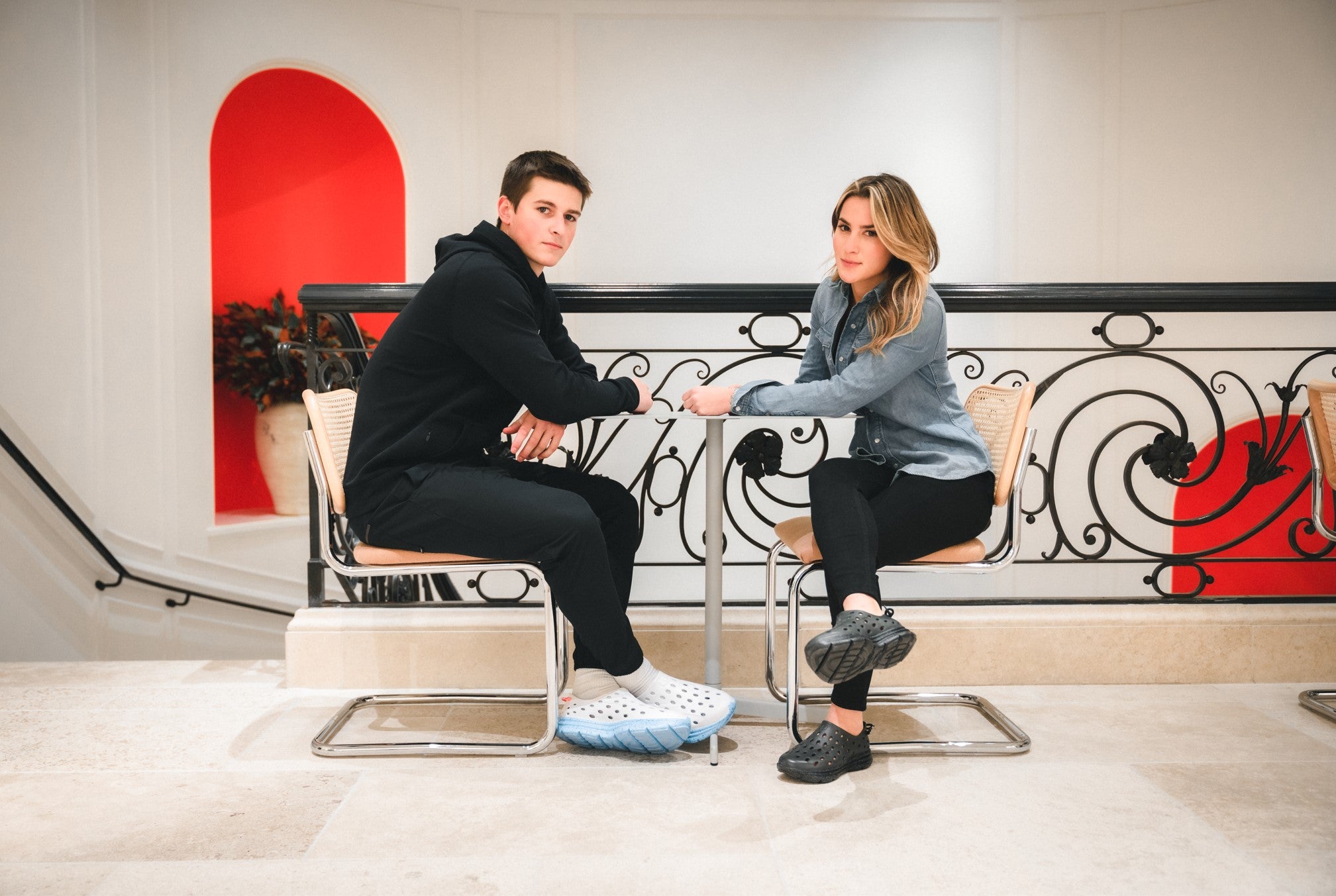 A man and a woman sitting at a table and showing off their comfortable indoor work shoes, Kane Revives.