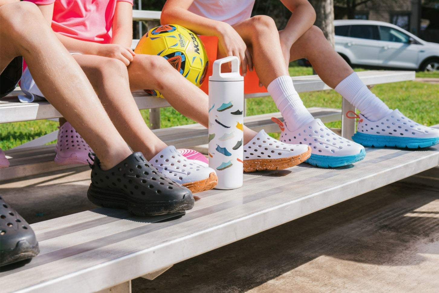 Closeup of Kids sitting at the bleachers, wearing different styles of Kane Revive recovery shoes for kids, available in fun colors