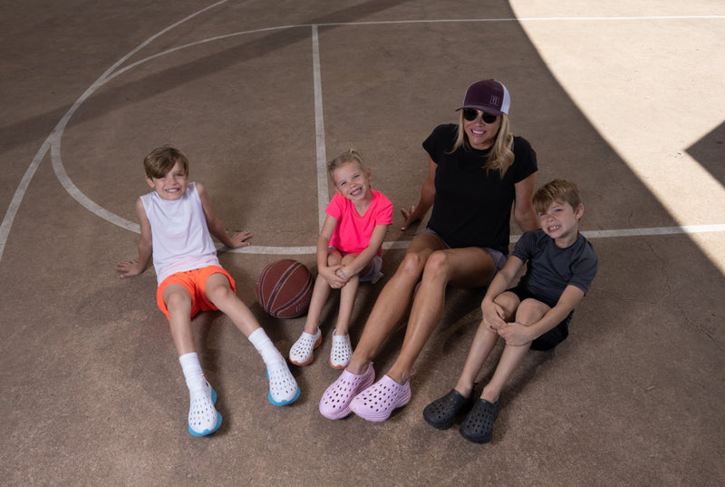 Kids smiling and posing with their mom at basketball practice. All of them are wearing brand new Kane Revive recovery shoes.