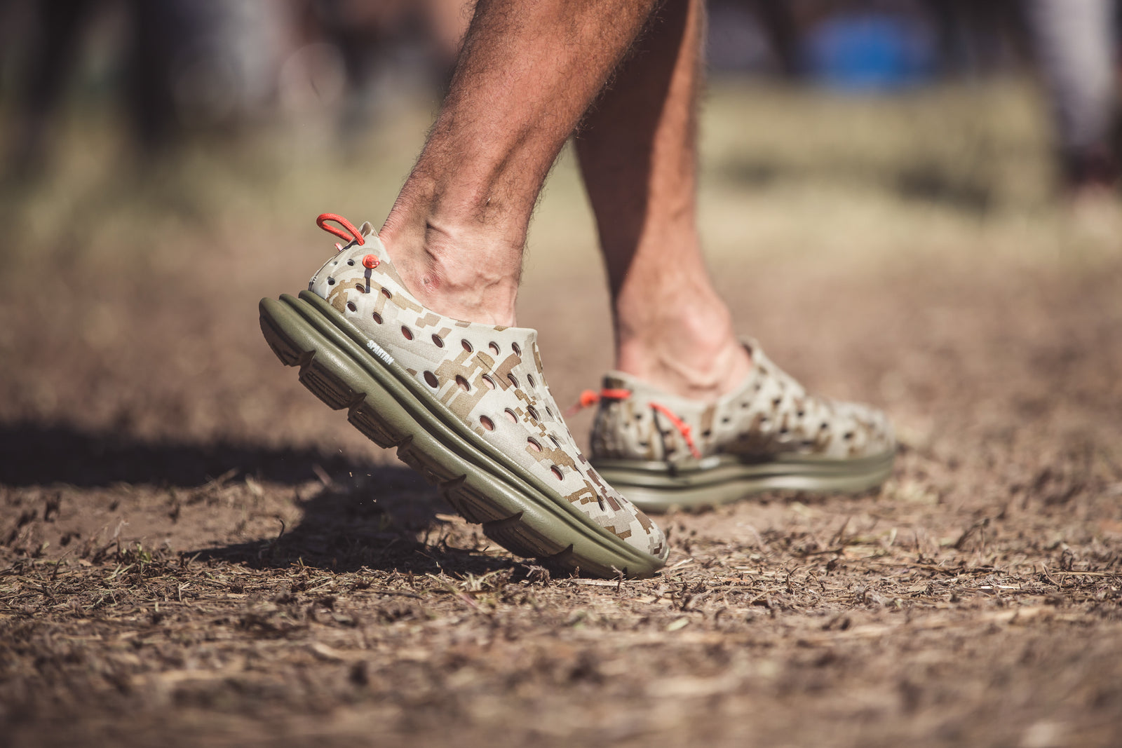 Close-up of feet walking on dry grass. Wearing Kane special edition recovery shoes. Focusing on the side profile of the camo-themed shoes.