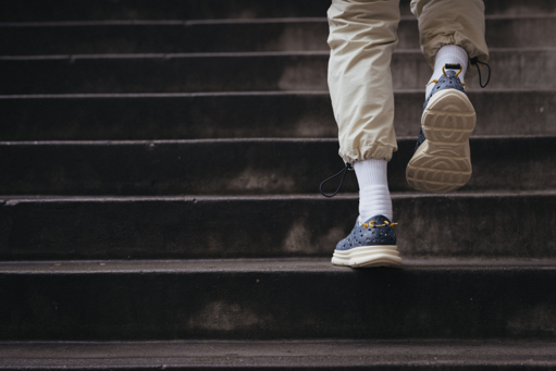 A delivery driver walking up stairs wearing Blue and White Kane Revive recovery shoes. Offering superior comfort and flexibility which is perfect for drivers who need to sit, walk, and drive all day.