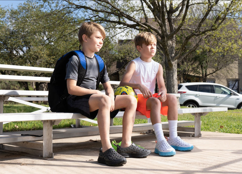 Kids at the park sitting on a bench wearing Kane Revive recovery shoes