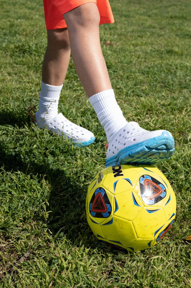 Closeup of a kid placing his foot on top of a soccer ball. Showcasing his stylish Kane Revive recovery shoes