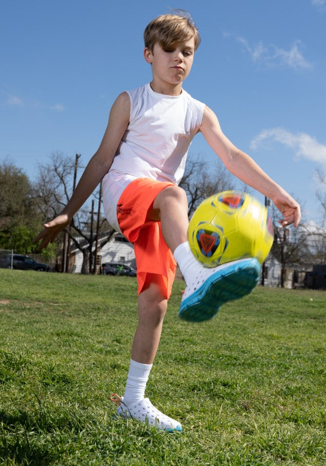 A kid kicking a soccer ball with his stylish Kane Revive recovery shoes for kids