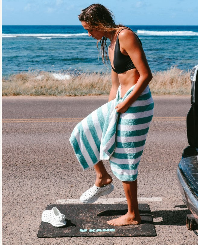 A woman getting changed at the beach, putting on her White Kane Revive recovery shoes after a surf session.
