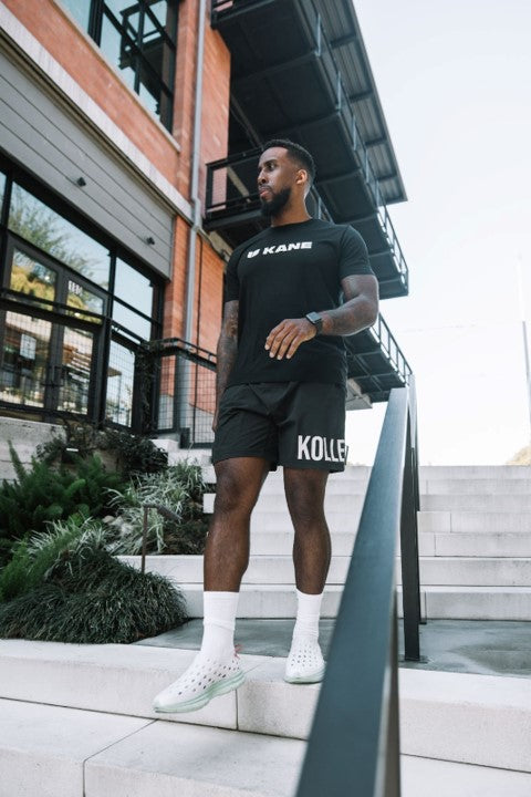 A man walking down the stairs wearing White Kane Revive recovery shoes. He's also wearing a stylish Kane Supima tee.