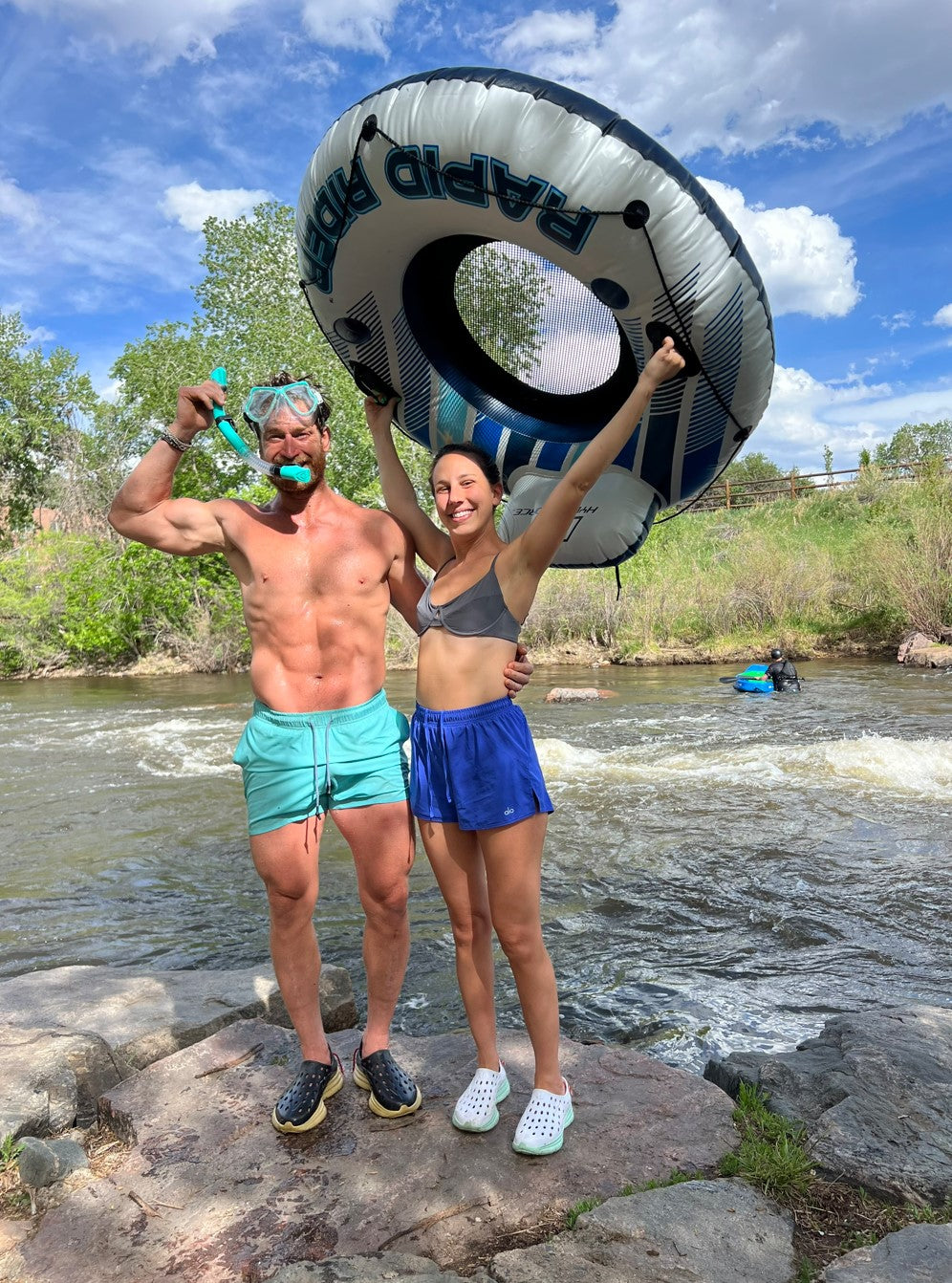 A man and a woman posing by the lake with their water tube. They are both wearing Kane Revive recovery shoes which are water-proof and retain grip even when wet.